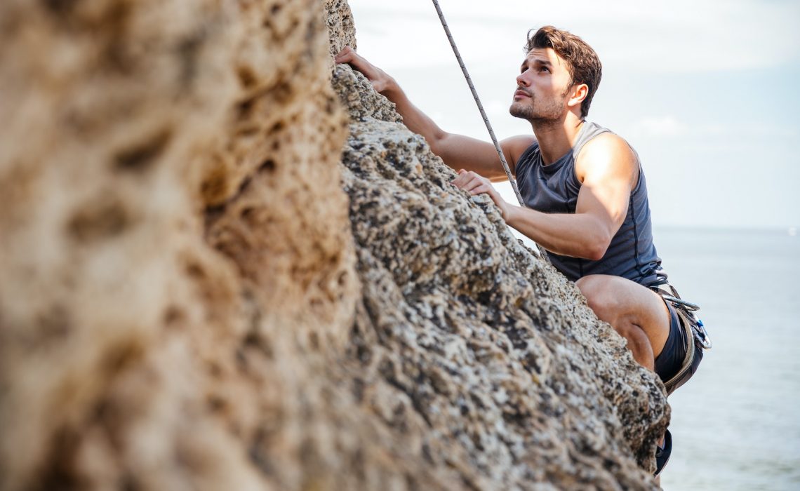 Young man climbing natural rocky wall Young man climbing natural rocky wall